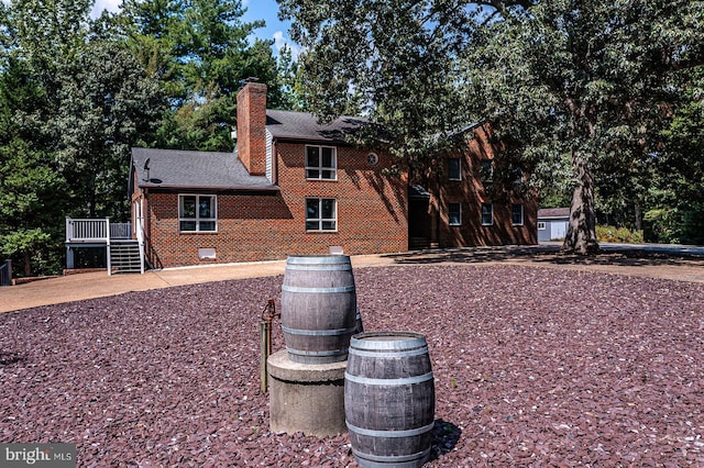 view of home's exterior featuring a deck, roof with shingles, brick siding, and a chimney