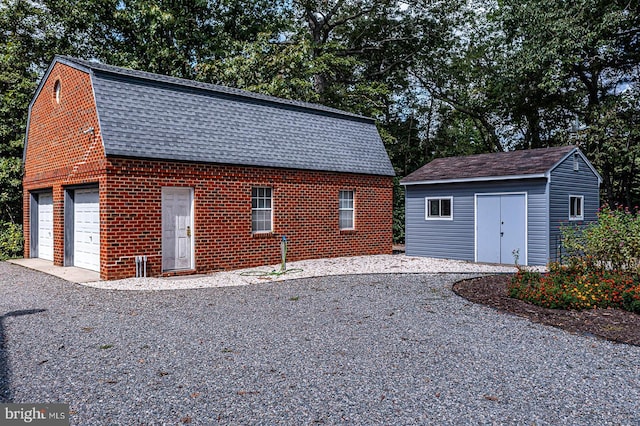 view of property exterior with a garage, a shingled roof, a gambrel roof, an outbuilding, and brick siding