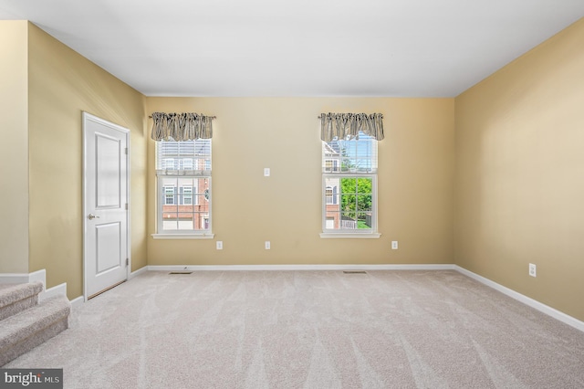 carpeted spare room with baseboards, visible vents, and plenty of natural light