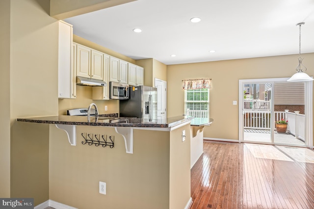 kitchen with a breakfast bar area, light wood-style flooring, stainless steel appliances, a peninsula, and under cabinet range hood