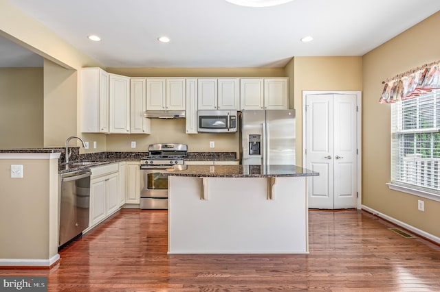 kitchen featuring a breakfast bar, a sink, stainless steel appliances, under cabinet range hood, and a kitchen island