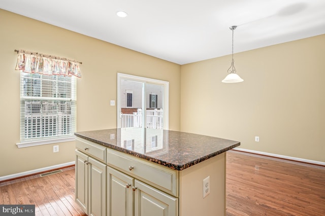 kitchen with hanging light fixtures, light wood finished floors, a center island, baseboards, and visible vents