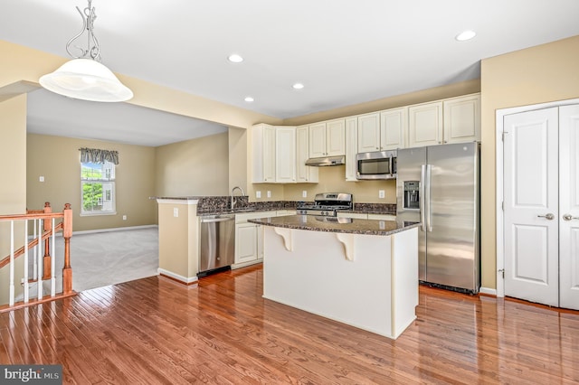 kitchen with a breakfast bar area, stainless steel appliances, wood finished floors, and under cabinet range hood