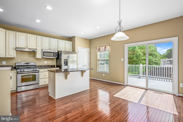 kitchen with a kitchen breakfast bar, a kitchen island, dark wood-style flooring, under cabinet range hood, and stainless steel appliances