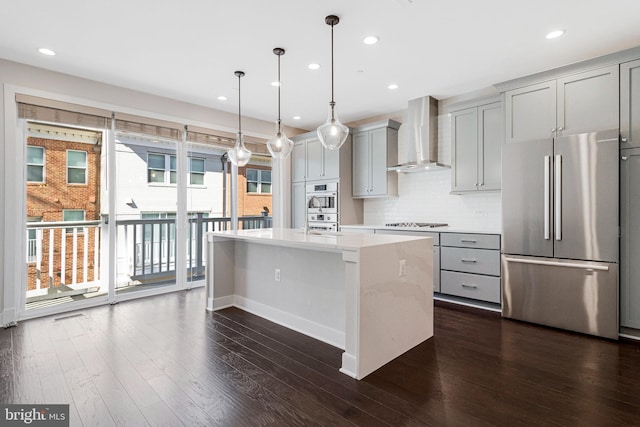 kitchen with gray cabinetry, an island with sink, gas stovetop, freestanding refrigerator, and wall chimney range hood