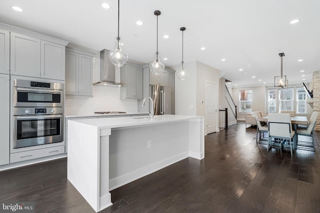 kitchen with a sink, light countertops, appliances with stainless steel finishes, wall chimney exhaust hood, and tasteful backsplash