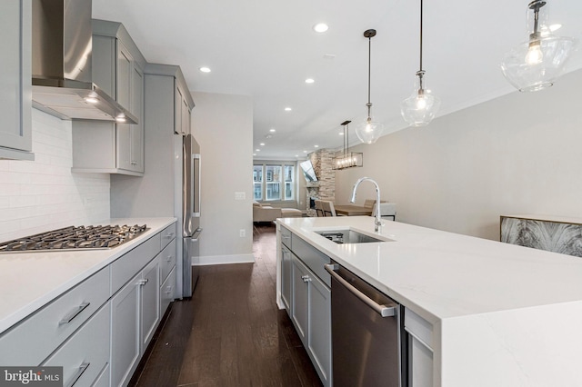 kitchen with gray cabinetry, stainless steel appliances, wall chimney exhaust hood, and a sink