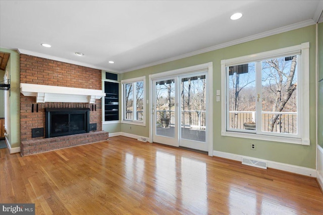 unfurnished living room featuring a fireplace, wood finished floors, visible vents, baseboards, and ornamental molding