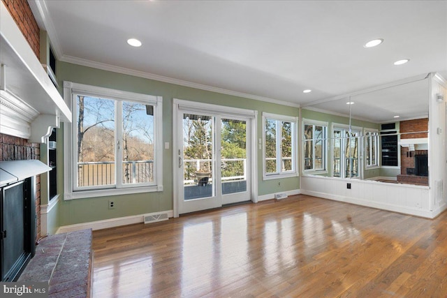 unfurnished living room featuring a brick fireplace, wood finished floors, visible vents, and crown molding