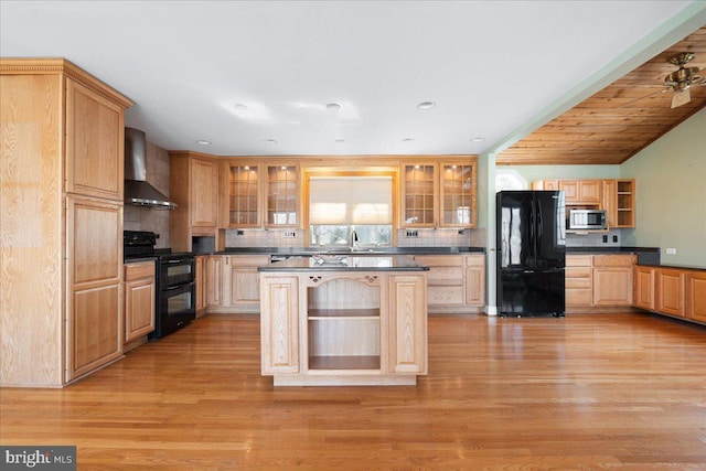 kitchen with wall chimney range hood, light wood-type flooring, black appliances, dark countertops, and glass insert cabinets