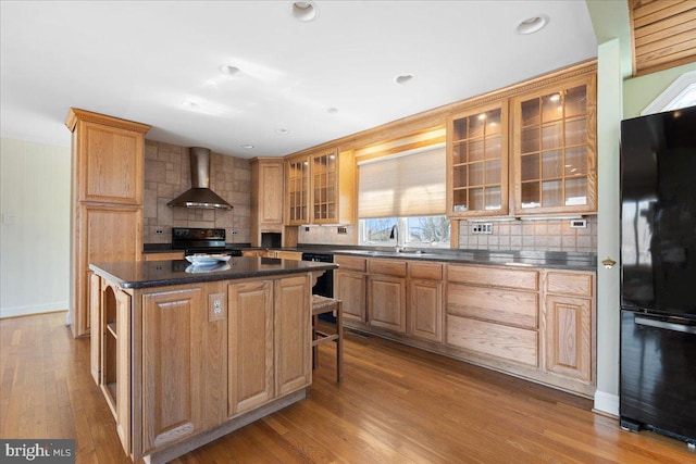 kitchen with a kitchen breakfast bar, black appliances, wall chimney exhaust hood, and wood finished floors