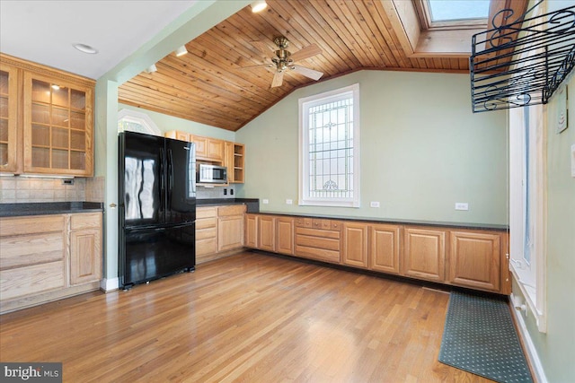 kitchen featuring stainless steel microwave, dark countertops, light brown cabinets, and freestanding refrigerator