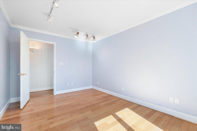 empty room with baseboards, track lighting, wood finished floors, and crown molding