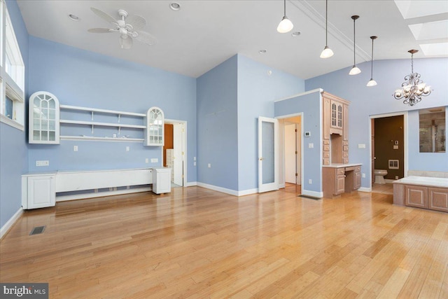 unfurnished living room with high vaulted ceiling, ceiling fan with notable chandelier, a skylight, visible vents, and light wood-type flooring