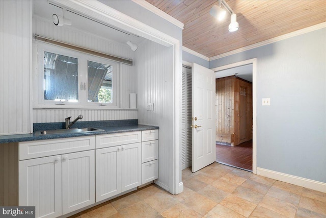 kitchen featuring baseboards, dark countertops, wooden ceiling, ornamental molding, and a sink