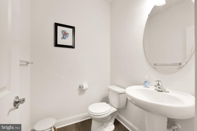 half bath featuring a sink, wood finished floors, toilet, and baseboards