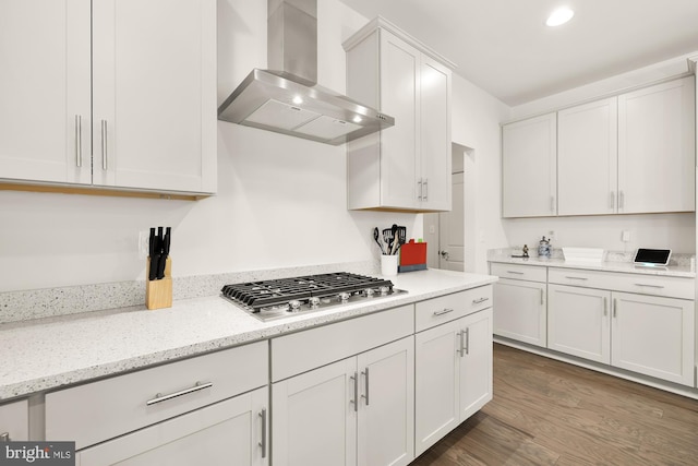 kitchen featuring dark wood-style floors, light stone counters, stainless steel gas cooktop, white cabinetry, and wall chimney range hood