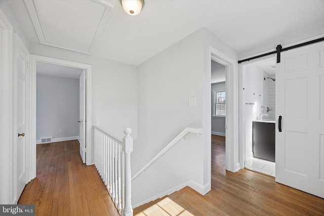 hall with visible vents, attic access, a barn door, an upstairs landing, and wood finished floors