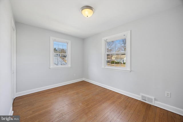 empty room featuring visible vents, baseboards, and hardwood / wood-style flooring