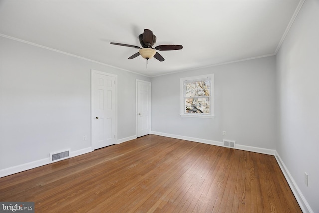 empty room featuring crown molding, baseboards, visible vents, and wood-type flooring