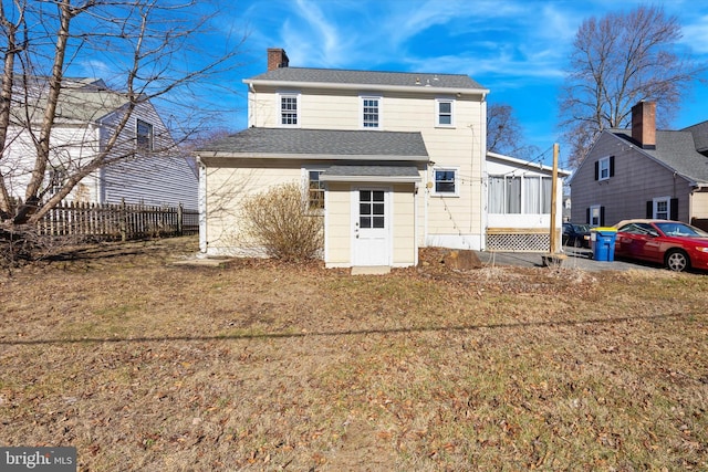 back of property with fence, roof with shingles, a chimney, a yard, and a sunroom