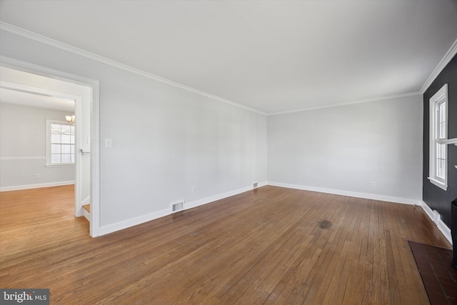 empty room featuring hardwood / wood-style floors, crown molding, baseboards, and visible vents