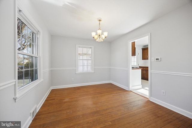 empty room featuring baseboards, visible vents, wood-type flooring, and an inviting chandelier