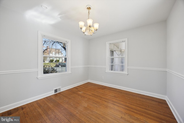 unfurnished room with an inviting chandelier, baseboards, visible vents, and wood-type flooring