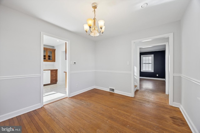 empty room with a chandelier, visible vents, baseboards, and wood-type flooring