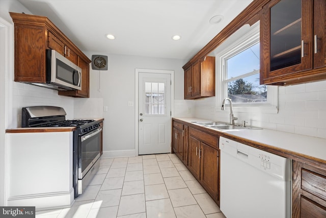 kitchen with a sink, light countertops, glass insert cabinets, appliances with stainless steel finishes, and backsplash