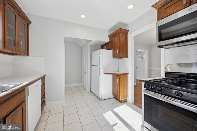 kitchen with tasteful backsplash, glass insert cabinets, light countertops, recessed lighting, and stainless steel appliances