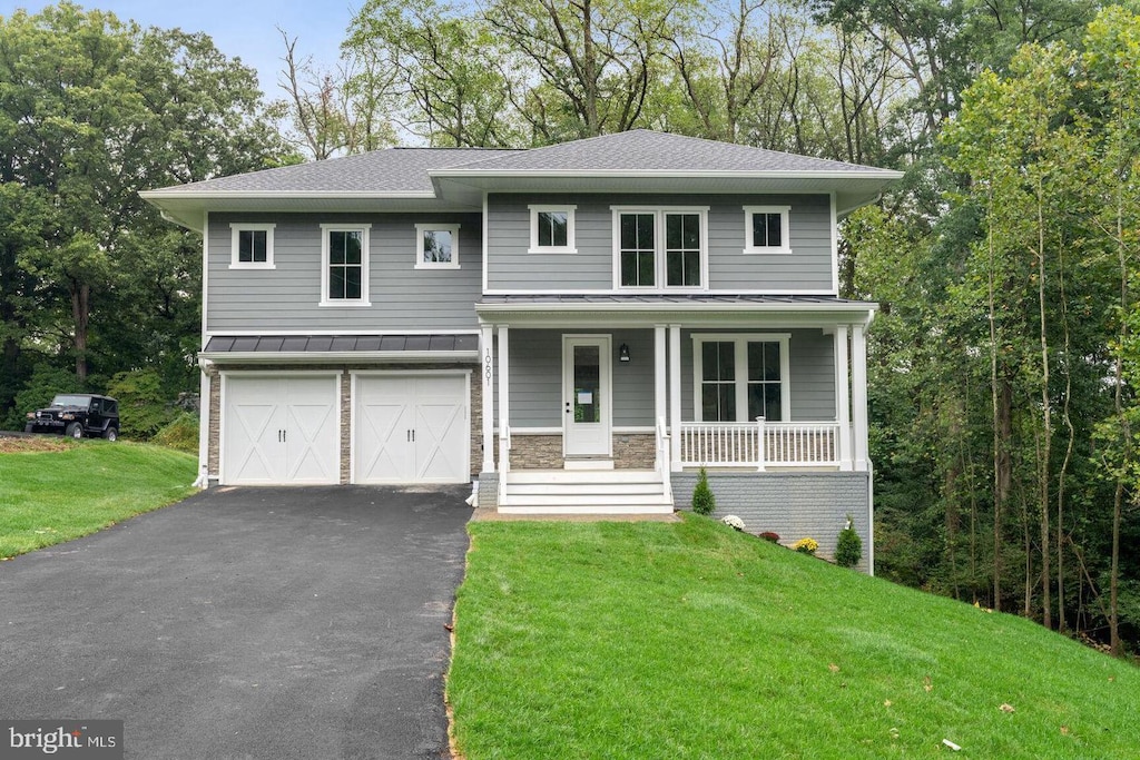 view of front of home featuring aphalt driveway, an attached garage, a shingled roof, a standing seam roof, and a front yard