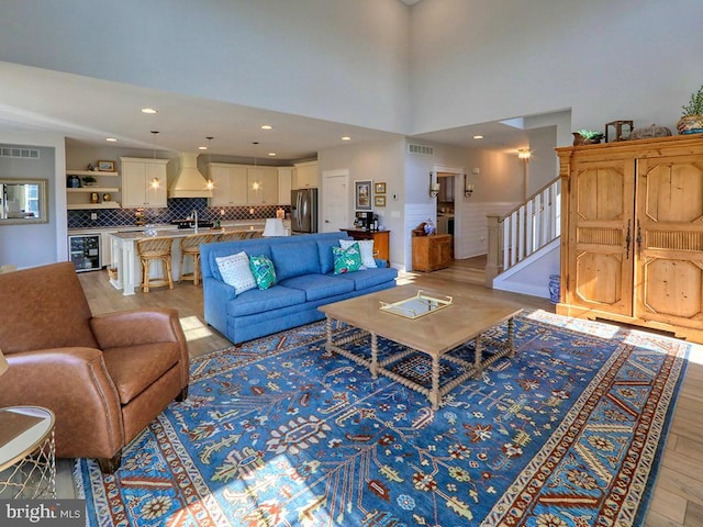 living room featuring beverage cooler, light wood finished floors, stairway, and visible vents