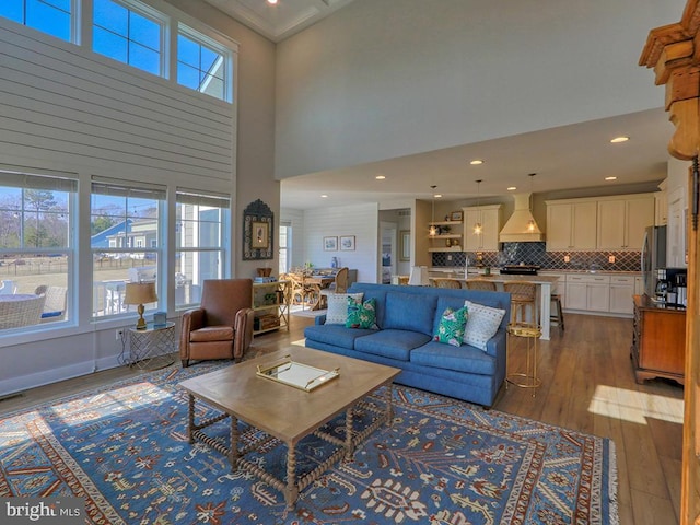 living room featuring recessed lighting, wood-type flooring, plenty of natural light, and a towering ceiling