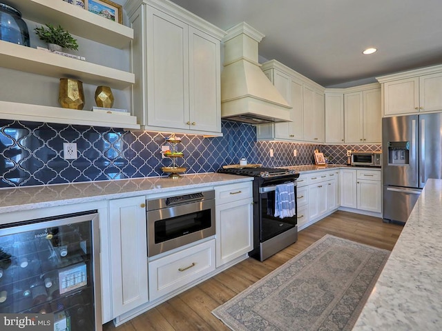 kitchen featuring custom exhaust hood, stainless steel appliances, light wood-style flooring, backsplash, and beverage cooler