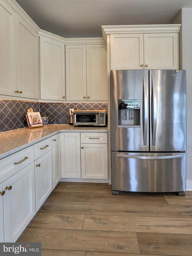 kitchen with white cabinetry, stainless steel fridge with ice dispenser, light wood finished floors, light stone countertops, and tasteful backsplash