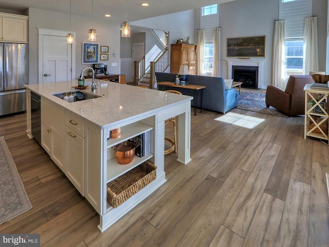 kitchen with a sink, open shelves, wood-type flooring, and stainless steel refrigerator