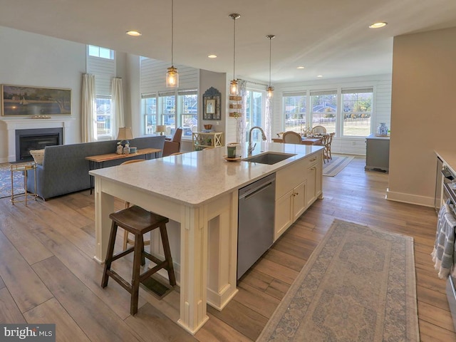 kitchen with dishwasher, wood finished floors, a sink, and a kitchen island with sink