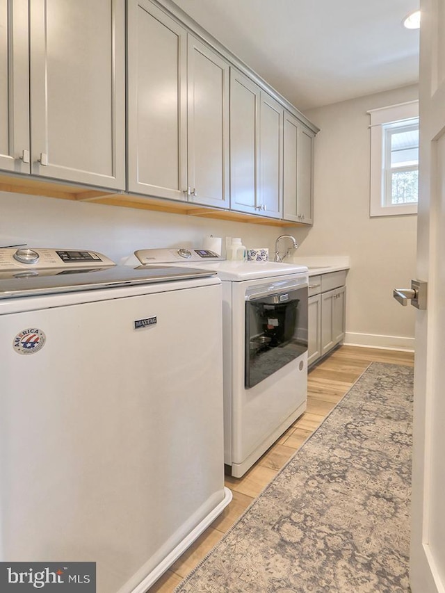 laundry area featuring light wood finished floors, washing machine and clothes dryer, cabinet space, and baseboards