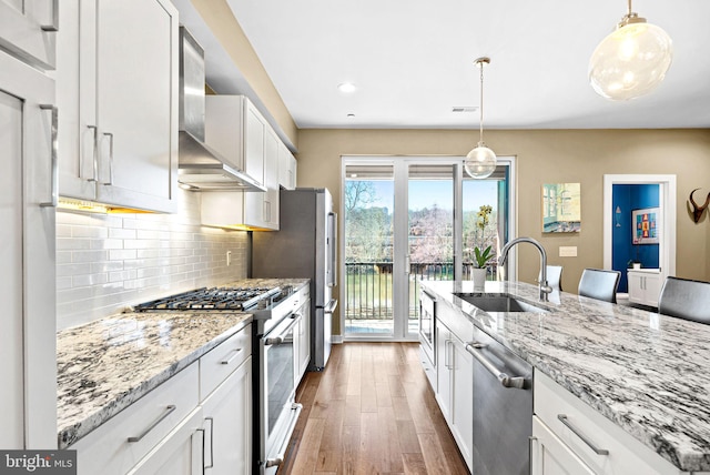 kitchen featuring wood finished floors, a sink, white cabinets, appliances with stainless steel finishes, and wall chimney range hood