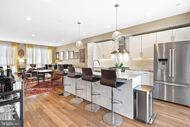 kitchen with white cabinetry, stainless steel refrigerator with ice dispenser, and wall chimney range hood