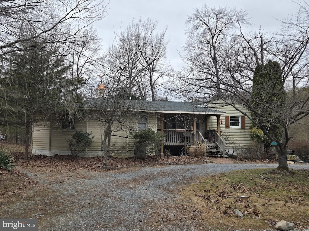 view of front facade with dirt driveway, a porch, and a chimney