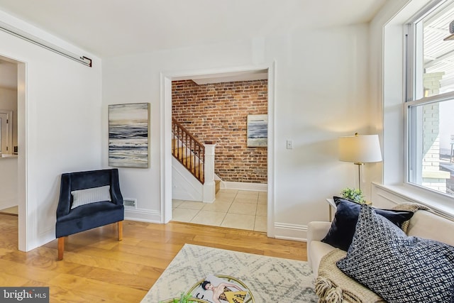 sitting room with stairs, brick wall, wood finished floors, and baseboards