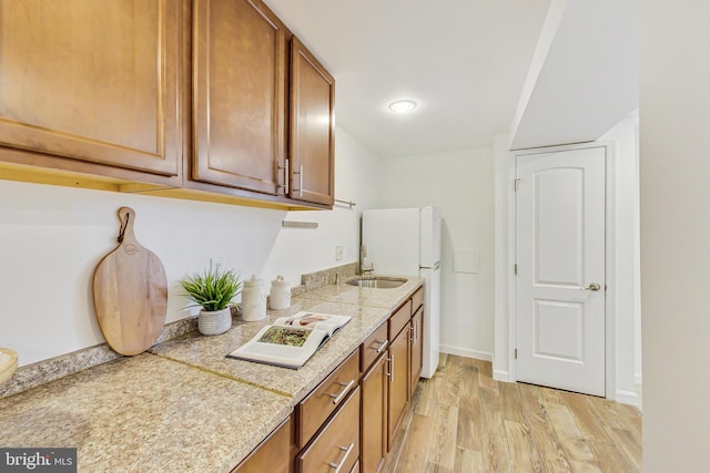 kitchen with light wood-style floors, baseboards, brown cabinets, and a sink