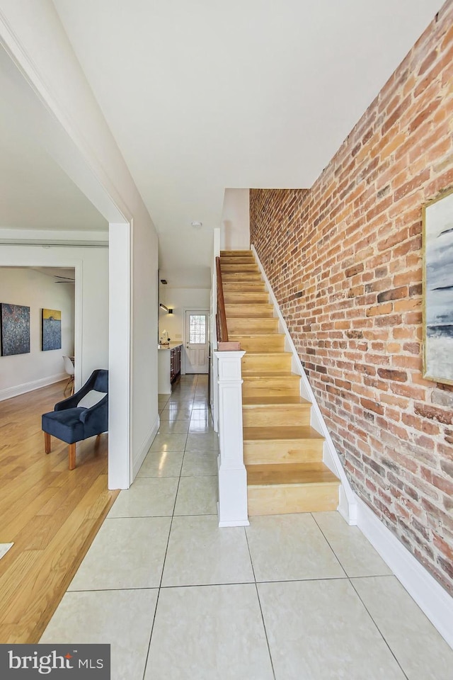 stairs with brick wall, tile patterned flooring, and baseboards