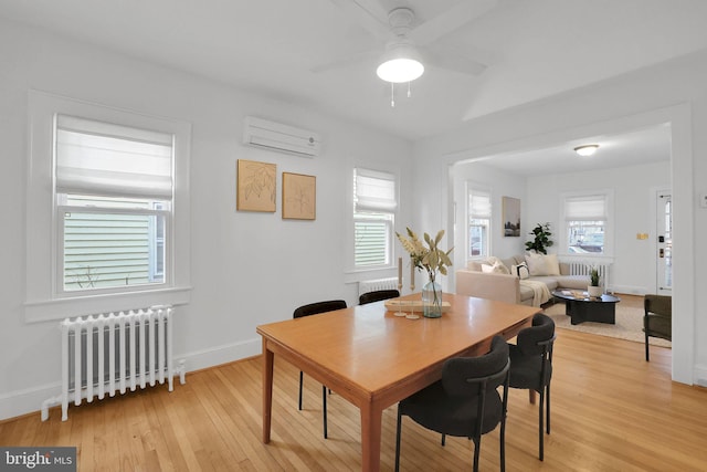 dining room featuring light wood finished floors, radiator heating unit, a ceiling fan, an AC wall unit, and baseboards