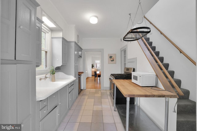 kitchen with white microwave, light tile patterned flooring, butcher block counters, gray cabinets, and stainless steel gas stove