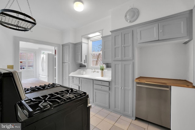 kitchen with light tile patterned floors, freestanding refrigerator, light countertops, gray cabinetry, and black gas stove