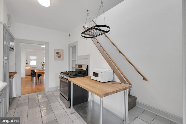 kitchen with gas range, light tile patterned floors, white microwave, and wooden counters