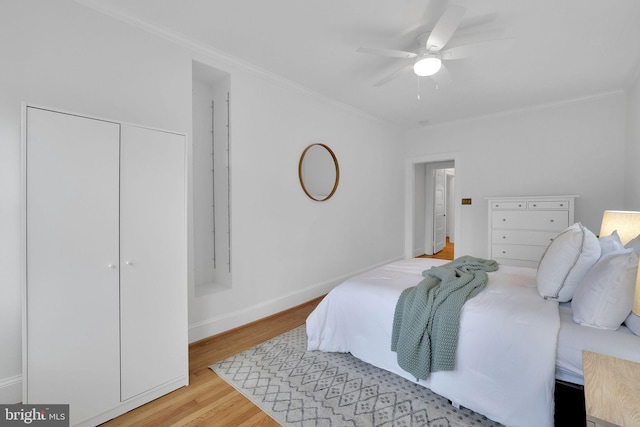 bedroom featuring wood finished floors, a ceiling fan, baseboards, a closet, and crown molding